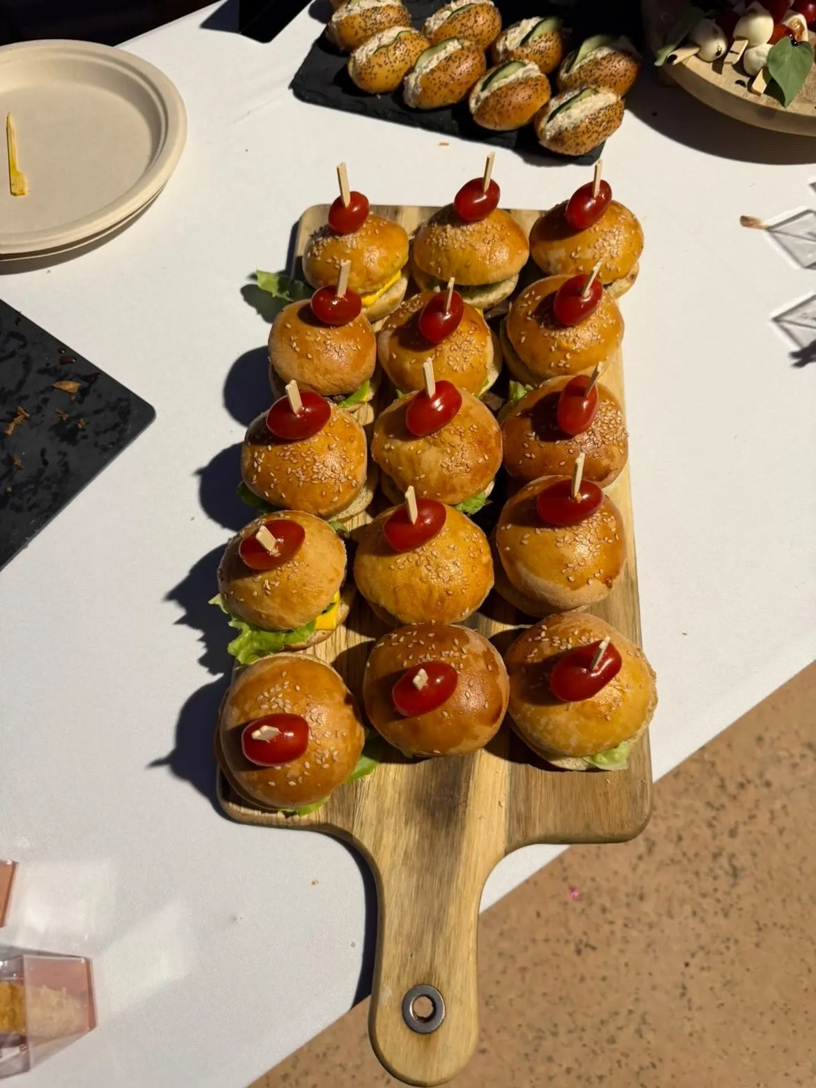 Mini-burgers piqués d'une tomate cerise, alignés sur une planche en bois